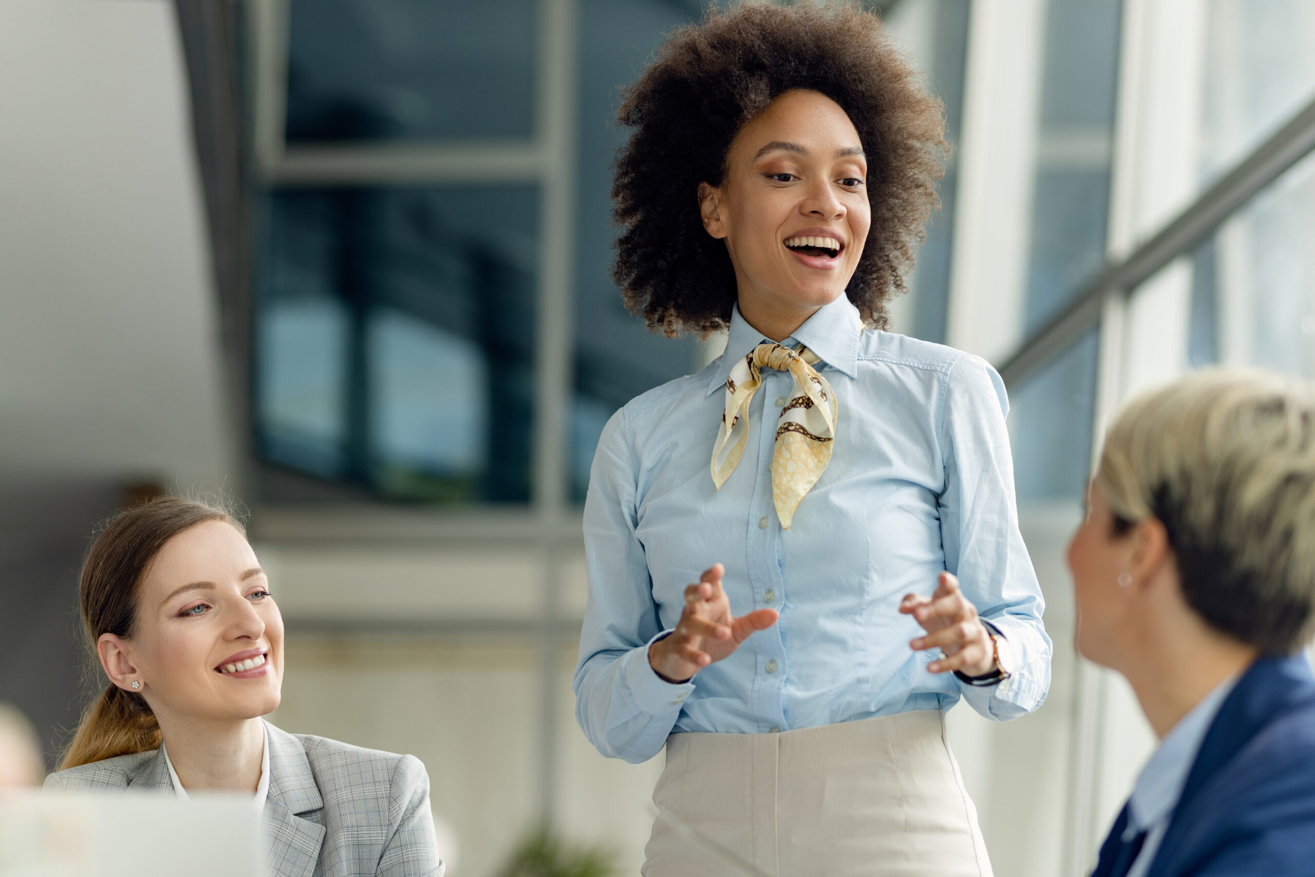 Happy black female entrepreneur talking to female coworkers while having business meeting in the office.